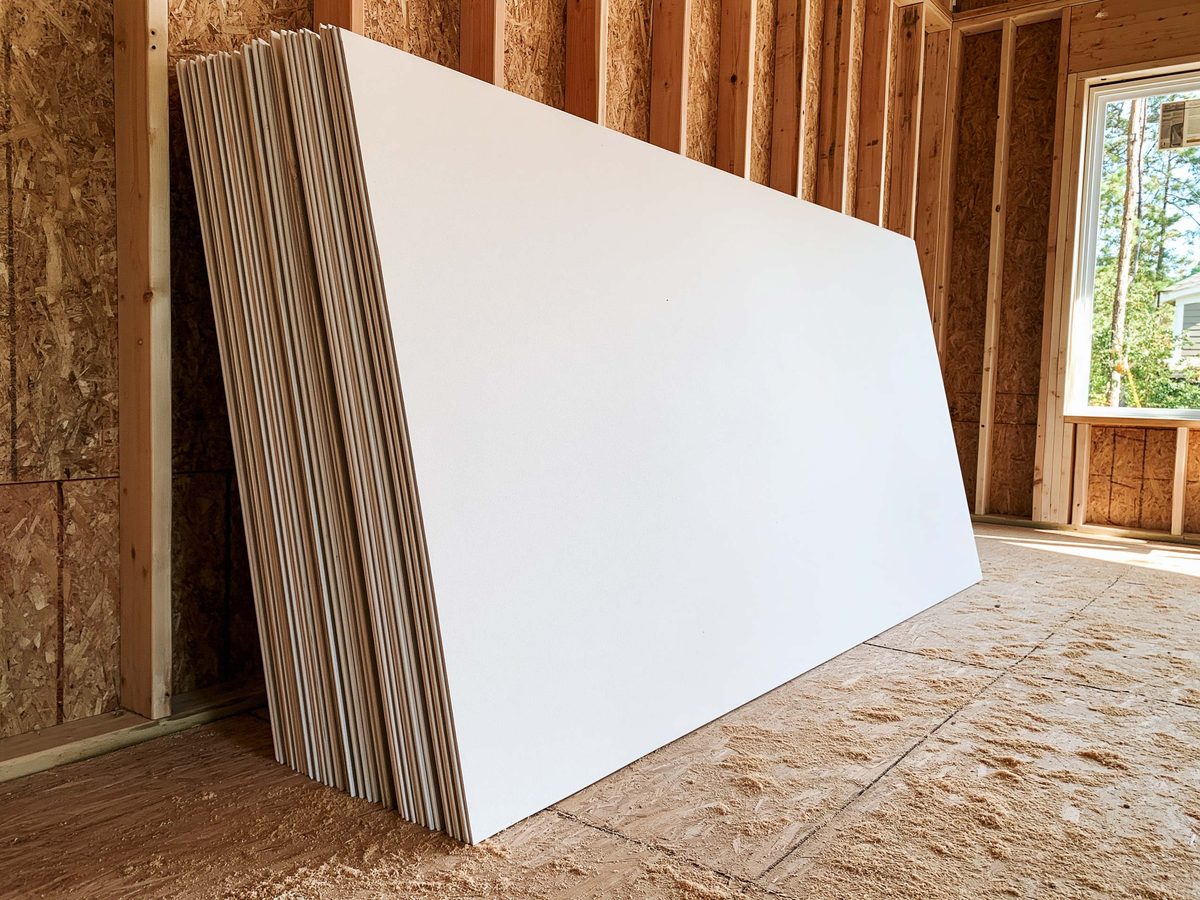A stack of new drywall sheets leaning against the framing of a room being built, sawdust across the subfloor