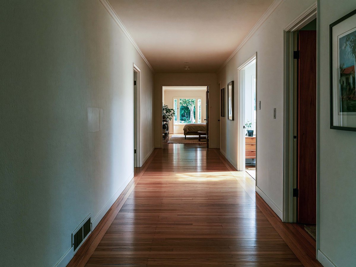 A hallway of an older Sacramento home looking through to a sunlit bedroom, one pale patch of filler on the left wall at waist height